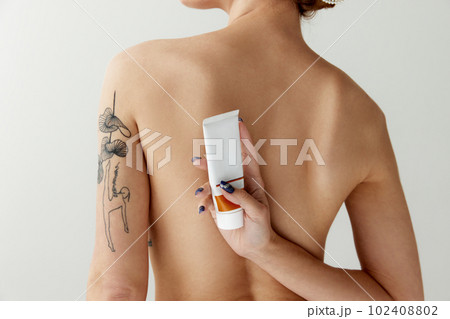 Back view cropped photo of female body with bare shoulders holding sunscreen, lotion, cream over white color studio background 102408802