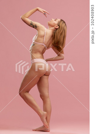 Side portrait with sensual slender girl with soft hair wearing beige underwear posing over pink background. Female fitness program 102408903