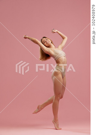 Portrait with beautiful slim girl, model wearing beige seamless underwear posing on fingertips over pink studio background. Beauty and wellness Portrait with beautiful slim girl, model wearing beige seamless underwear posing on fingertips over pink studio background. Beauty and wellness 102408979