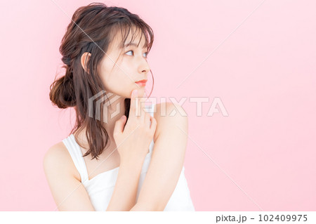 ピンクバックでスキンケアをする若い女性 102409975