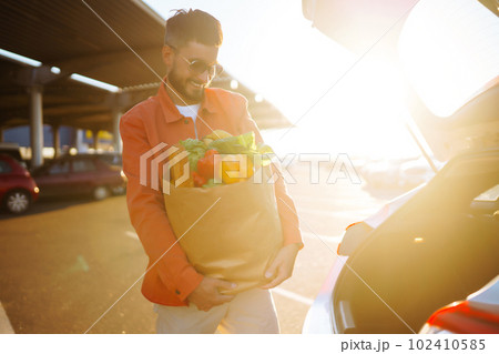 Young man with shopping bag full of vegetables near the car. Handsome man after shopping. 102410585