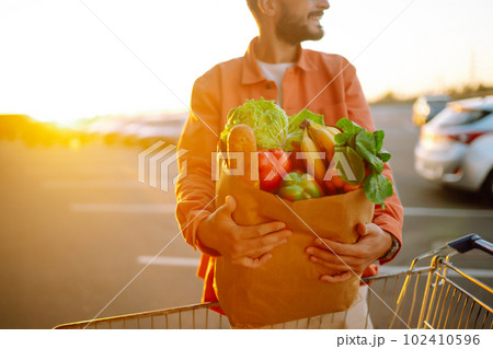 Young man with shopping bag full of vegetables near the car. Handsome man after shopping. Young man with shopping bag full of vegetables near the car. Handsome man after shopping. 102410596