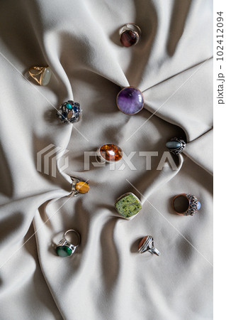 Many different silver rings with various natural gemstones on a beige background. 102412094