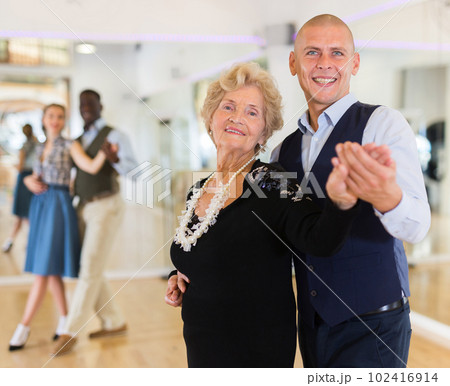Man and elderly woman performing ballroom dance in dancing room 102416914