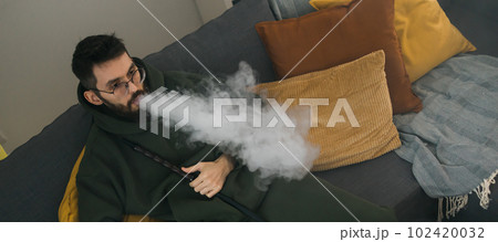 Banner bearded millennial or gen z man smoking hookah while relaxing on sofa at home copy space - chill time and resting concept 102420032