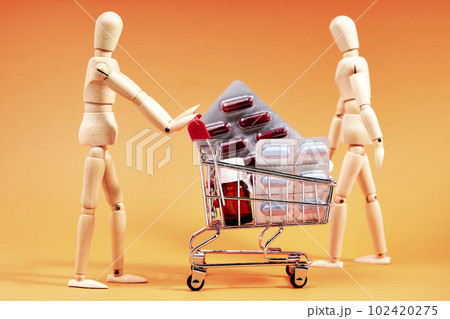 Dummy pushing a shopping trolley with medicines on an orange background. Medicine concept 102420275