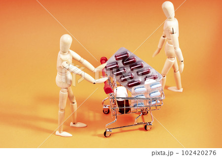 Dummy pushing a shopping trolley with medicines on an orange background. Health concept 102420276
