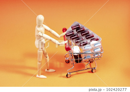 Dummy pushing a shopping trolley with medicines on an orange background. Medicine concept 102420277