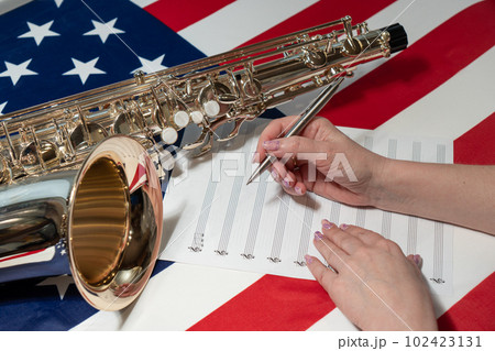 Female hands writing musical notes on a sheet of sheet music, against the background of the American flag, The concept of creating music 102423131