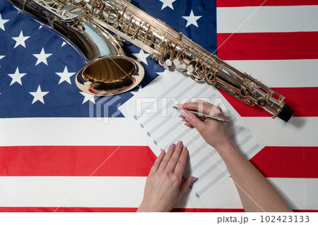 Female hands writing musical notes on a sheet of sheet music, against the background of the American flag, The concept of creating music 102423133
