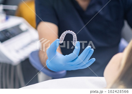 Professional orthodontist showing innovative aligners designed for bite correction to camera doctor in rubber gloves demonstrates modern transparent caps for teeth 102428566