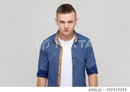 Portrait of enraged furious attractive teenager boy wearing blue shirt standing looking at camera, expressing wild anger and hate, feeling crazy. Indoor studio shot isolated on gray background. Portrait of enraged furious attractive teenager boy wearing blue shirt standing looking at camera, expressing wild anger and hate, feeling crazy. Indoor studio shot isolated on gray background. 102429293