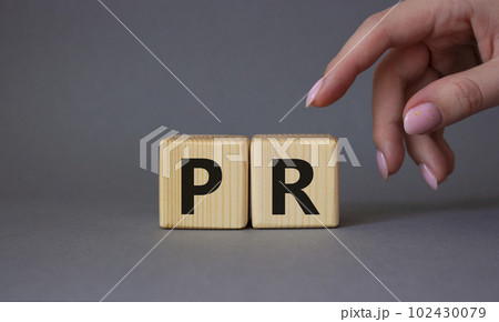 PR - Public Relations symbol. Concept word PR on wooden cubes. Businessman hand. Beautiful grey background. Business and PR concept. Copy space. 102430079