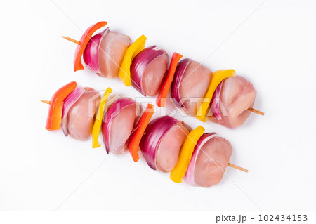 Uncooked mixed meat skewer with peppers.Skewers with pieces of raw meat, red, yellow and green pepper.Raw chicken leg meat skewers with vegetables, peppers, onions, on a white background.Top view. 102434153