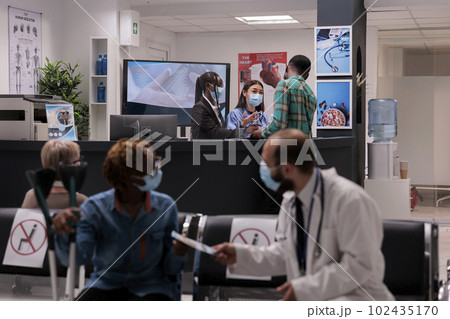Female hospital staff members attending a sick young african american man at reception area. Doctor handing prescription to woman with partial body paralysis. Medical clinic lobby during covid Female hospital staff members attending a sick young african american man at reception area. Doctor handing prescription to woman with partial body paralysis. Medical clinic lobby during covid 102435170