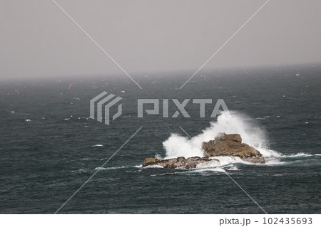 激しく白い波しぶきを上げ岩に波がぶつかる青い海面の海と水平線と空のある風景 激しく白い波しぶきを上げ岩に波がぶつかる青い海面の海と水平線と空のある風景 102435693