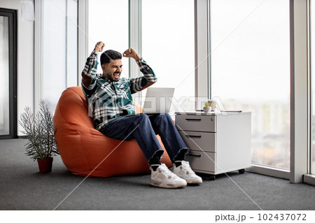 Excited hindu man celebrating success with laptop on knees Excited hindu man celebrating success with laptop on knees 102437072