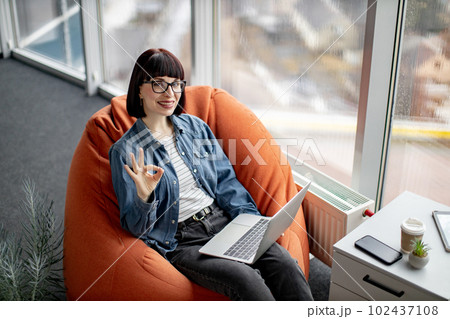 Charismatic lady working on laptop and smiling at camera 102437108