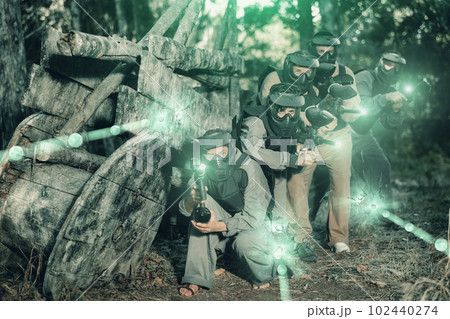 Paintball players of one team in camouflages and masks aiming with gun in shootout Paintball players of one team in camouflages and masks aiming with gun in shootout 102440274