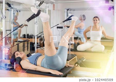 Woman exercising torson rotation at sport gym using pilates reformer beds 102440509