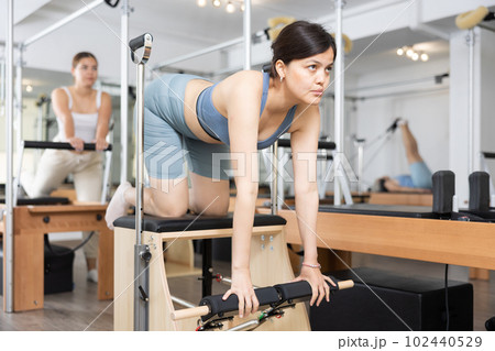 Young positive woman doing Pilates on special equipment in gym 102440529
