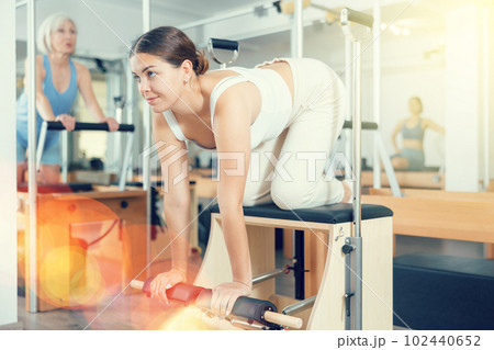 Young woman making pilates exercising while standing on knees using Wanda chair machine Young woman making pilates exercising while standing on knees using Wanda chair machine 102440652