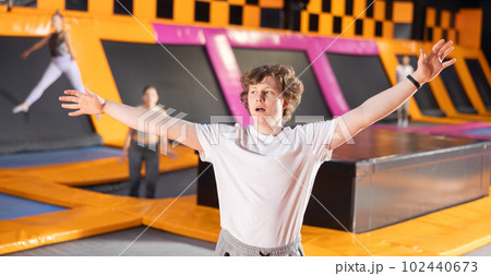 Teenage boy in sport clothes doing exercises in trampoline arena Teenage boy in sport clothes doing exercises in trampoline arena 102440673
