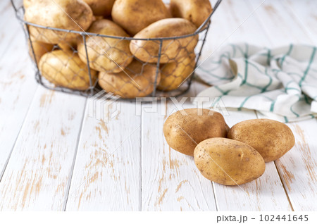 fresh organic potato on white wooden table with a potato metal basket in the background. fresh organic potato on white wooden table with a potato metal basket in the background. 102441645