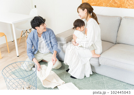 リビングで妻が子供の面倒を見ている間、洗濯物をたたんで家事に協力している夫 リビングで妻が子供の面倒を見ている間、洗濯物をたたんで家事に協力している夫 102445043