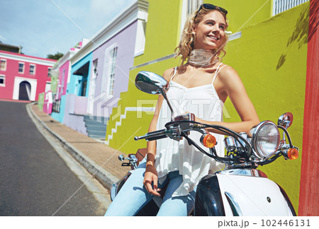 The city always puts a smile on her face. a young woman riding a scooter through colorful city streets. The city always puts a smile on her face. a young woman riding a scooter through colorful city streets. 102446131