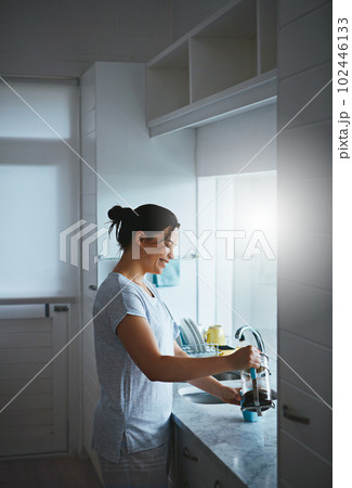 She couldnt wait for the fist cup of the day. an attractive young woman preparing a pot of coffee in the kitchen. 102446133