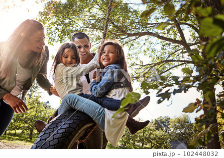 Making family memories. a happy mother and father pushing their daughters on a tyre swing. 102448032