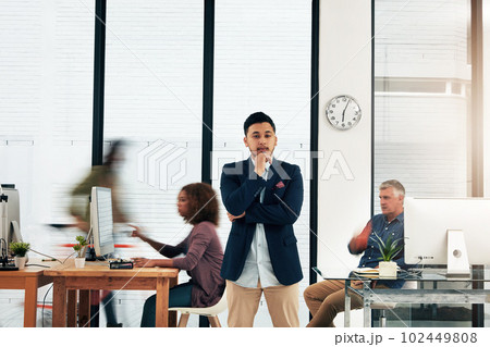 Hes young and full of ideas. Portrait of a young designer standing in the office with his colleagues in the background. 102449808