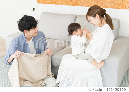 リビングで妻が子供の面倒を見ている間、洗濯物をたたんで家事に協力している夫 リビングで妻が子供の面倒を見ている間、洗濯物をたたんで家事に協力している夫 102450530