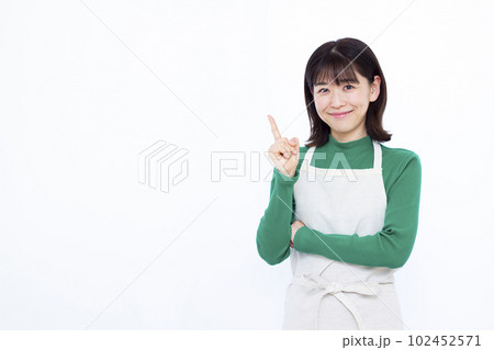 白い背景の前で人差し指を立てる30代のエプロン姿の主婦 102452571