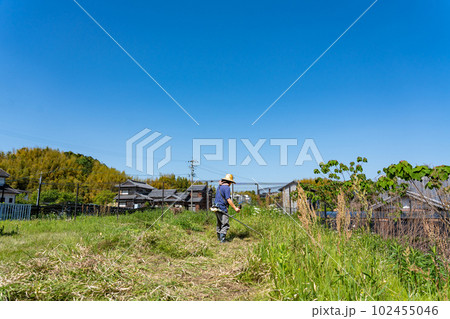 初夏に草刈り機で草刈りをする高齢男性 102455046