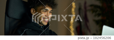 Cheerful young guy with piercing smiling while sitting in front of laptop screen late in the evening 102456206