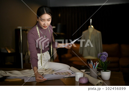 Beautiful Asian female tailor or fashion designer checking her new sketch design Beautiful Asian female tailor or fashion designer checking her new sketch design 102456899