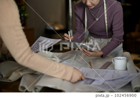 A fashion designer checking new clothes design on tablet and working with her team in the studio. A fashion designer checking new clothes design on tablet and working with her team in the studio. 102456900