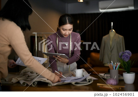 Professional Asian female fashion designer checking her new collection sketch with her team Professional Asian female fashion designer checking her new collection sketch with her team 102456901