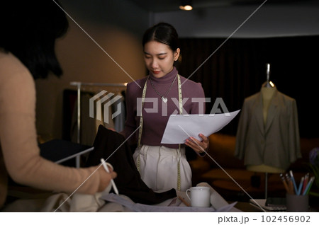 Professional Asian female fashion designer checking the quality of fabric with her team Professional Asian female fashion designer checking the quality of fabric with her team 102456902