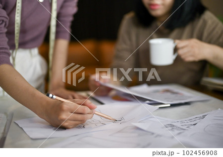 Two dressmakers sketching their new design and working in the studio together. Two dressmakers sketching their new design and working in the studio together. 102456908