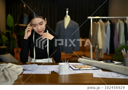Focused Asian female fashion designer working on her new clothes collection in a studio. Focused Asian female fashion designer working on her new clothes collection in a studio. 102456929