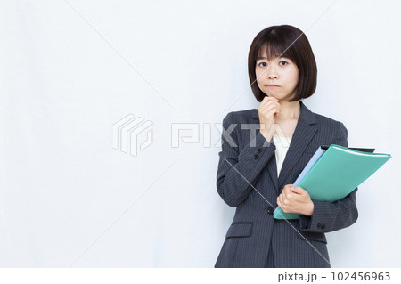 白い背景の前で悩んでいるスーツ姿の30代女性 白い背景の前で悩んでいるスーツ姿の30代女性 102456963