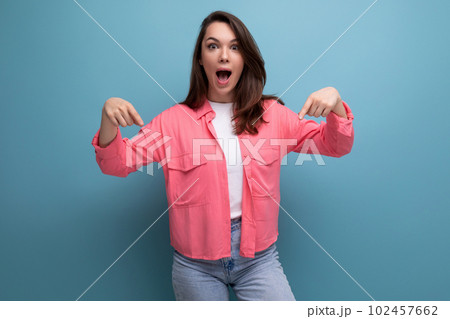 cheerful brunette lady in a pink shirt and jeans points her finger at the infomation on a studio cheerful brunette lady in a pink shirt and jeans points her finger at the infomation on a studio 102457662