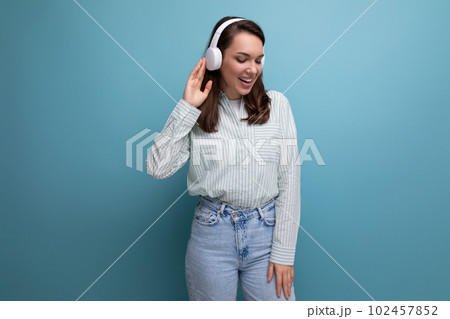 energetic pretty cute brunette young woman in shirt listening to music on studio background with 102457852