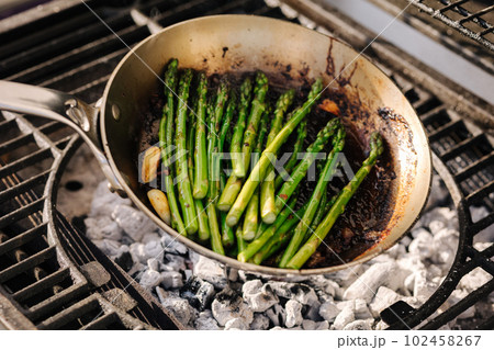 Delicious preparation of green asparagus cooked in butter with garlic in a frying pan on outdoor BBQ grill. Delicious preparation of green asparagus cooked in butter with garlic in a frying pan on outdoor BBQ grill. 102458267