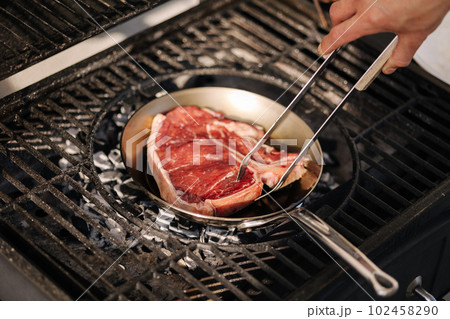 Human hand using grilling tongs to flip the steak on pan. Grill outdoor.  102458290