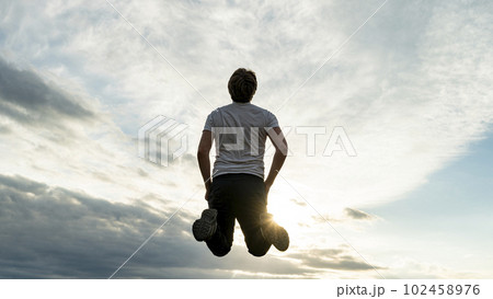 Low angle view of a man jumping up high in the air under a dramatic sky Low angle view of a man jumping up high in the air under a dramatic sky 102458976