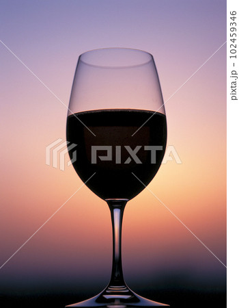 赤ワインの入ったワイングラスと夕景のグラデーション 赤ワインの入ったワイングラスと夕景のグラデーション 102459346
